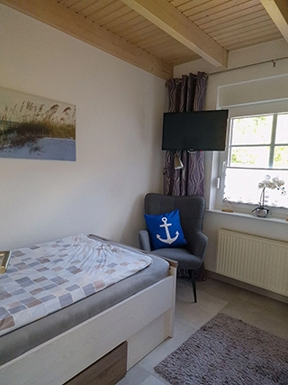 Schlafzimmer mit Sessel, Fenster und Wandfernseher
